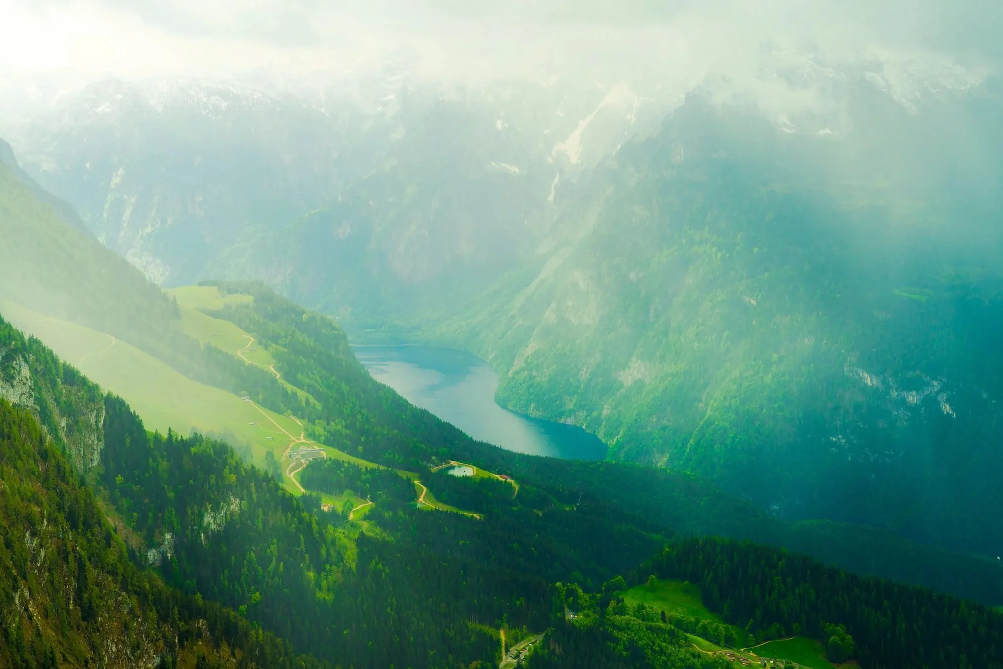 Steep green mountain walls closing in on a narrow blue lake far below, softened by summer haze.