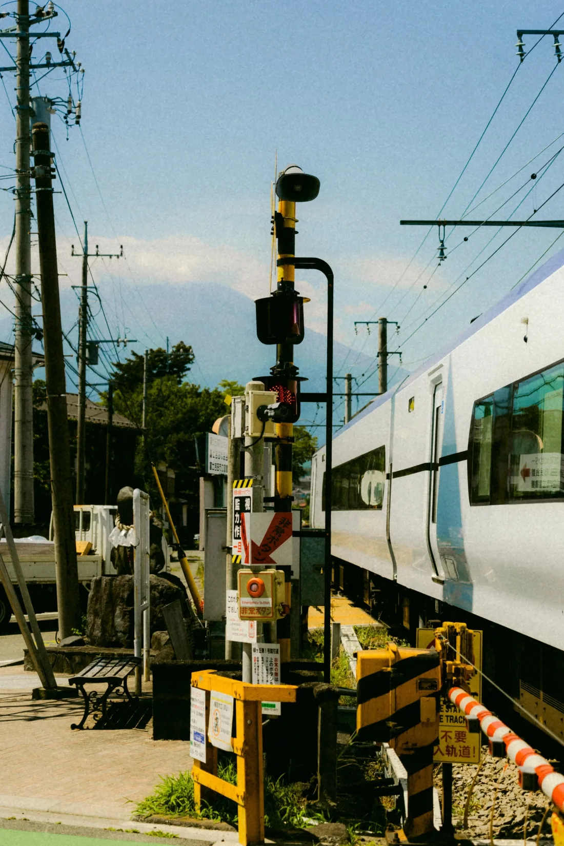 A commuter train passing a level crossing behind striped barriers, signal heads and overhead wires against pale sky.
